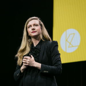 Kirryn on stage looking thoughtful in front of a yellow screen