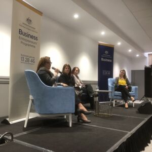 Kirryn sits on a stage as chair person with 3 women
