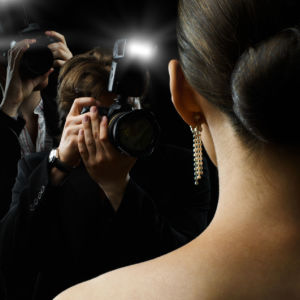 Back of a glamourous ladies head who is facing a pack of flashing photographers.