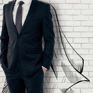 Man in a suit standing against a white brick wall with super hero cape behind.