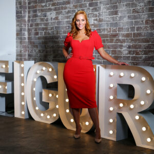 Jules in a red dress standing in front of a sign that says Figur